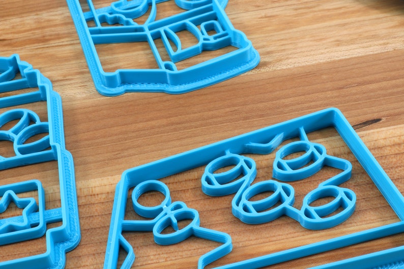 May include: Three blue plastic cookie cutters, one shaped like a house, one shaped like a star, and one shaped like a group of circles.