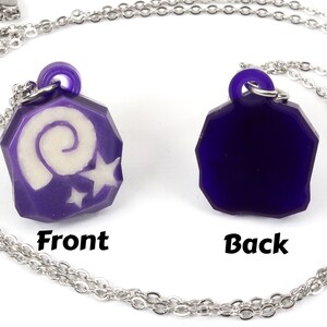 May include: A purple necklace with a pendant featuring a white spiral and stars. The back of the pendant is solid purple. The necklace is on a silver chain.