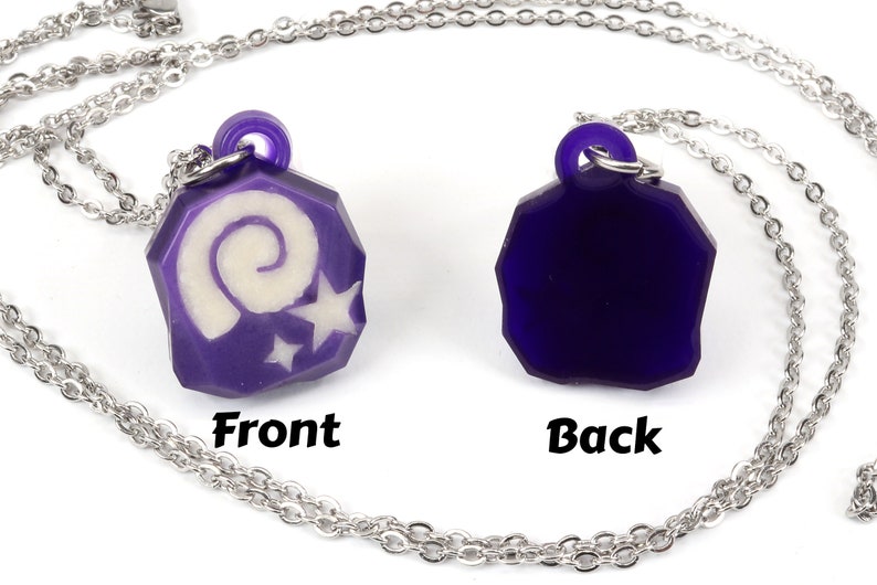 May include: A purple necklace with a pendant featuring a white spiral and stars. The back of the pendant is solid purple. The necklace is on a silver chain.