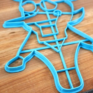 May include: A blue plastic cookie cutter shaped like a cartoon character. The cutter has a detailed design with multiple cutouts.