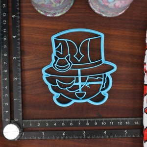 May include: A blue plastic cookie cutter shaped like a cartoon character wearing a hat. The character has a large hat with a brim and a small, round face with a smile.