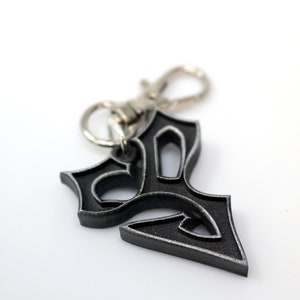 May include: A silver and black metal keychain with a stylized design. The keychain has a silver metal clasp.