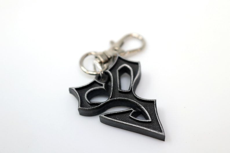 May include: A silver and black metal keychain with a stylized design. The keychain has a silver metal clasp.