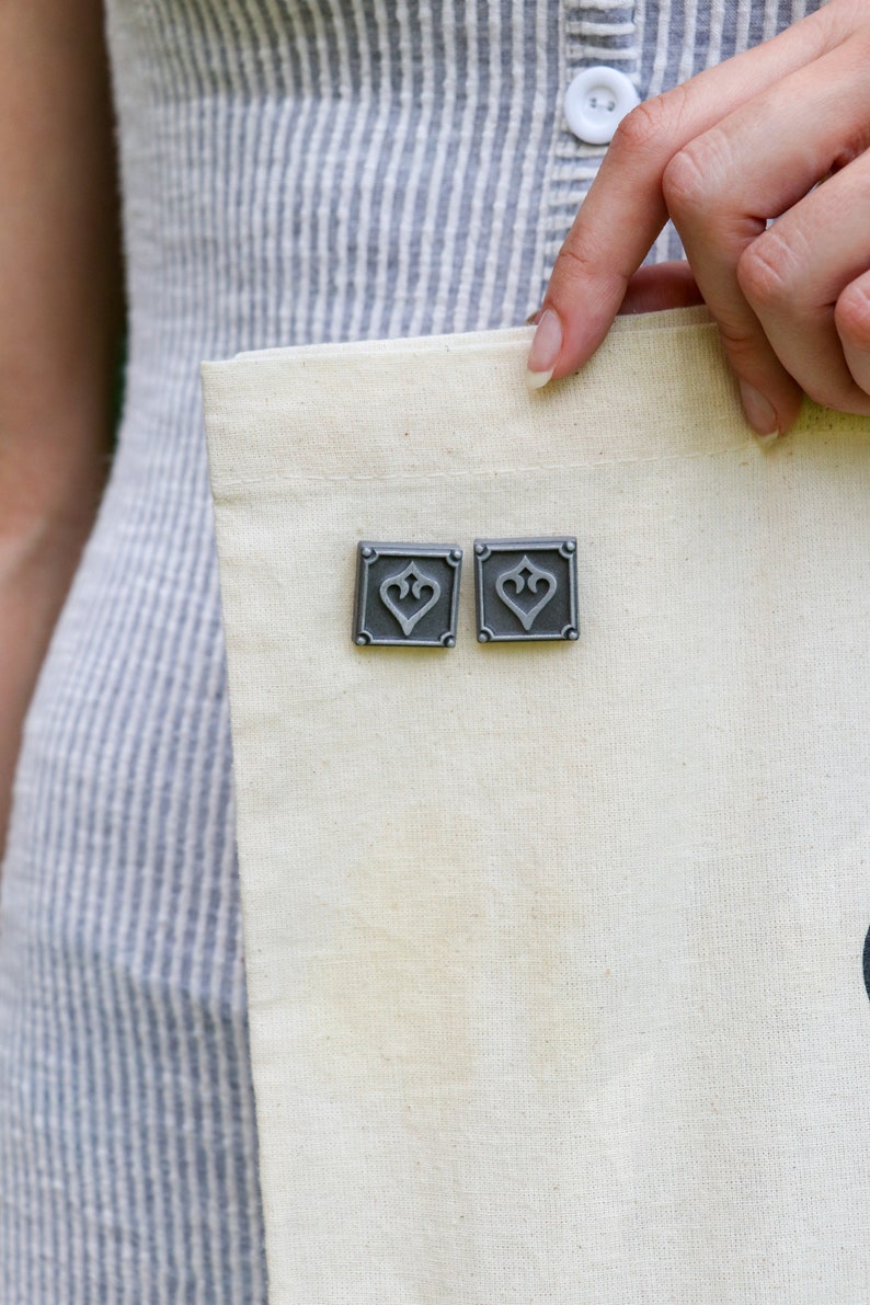 Peut inclure: Deux &eacute;pingles en m&eacute;tal argent&eacute; avec un motif de c&oelig;ur sur un sac fourre-tout en toile blanche.