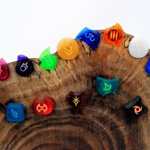 May include: A set of 14 colourful resin dice with various symbols and designs. The dice are arranged in a semi-circle on a wooden surface.