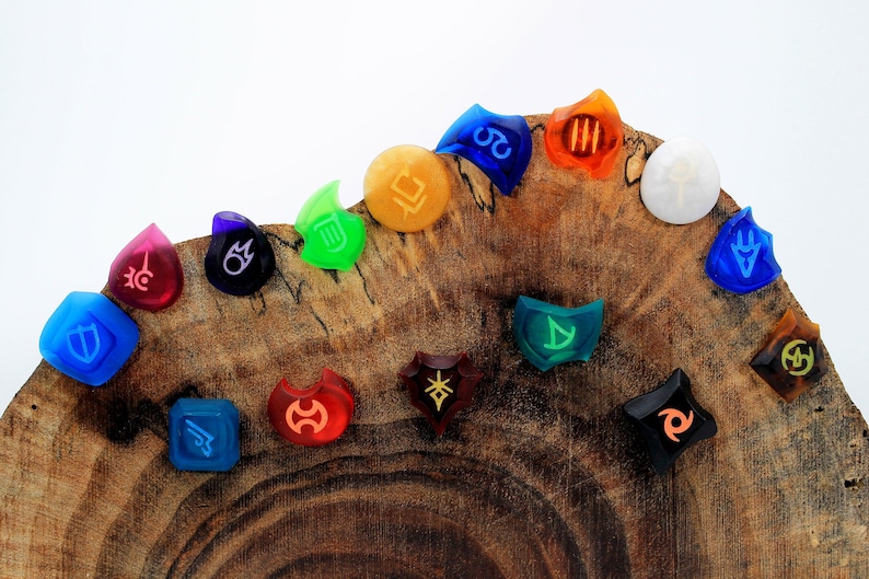 May include: A set of 14 colourful resin dice with various symbols and designs. The dice are arranged in a semi-circle on a wooden surface.
