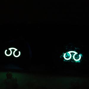 May include: Two dark objects with a glowing green symbol of three interlocking circles. The symbol is a common symbol in fantasy and science fiction.