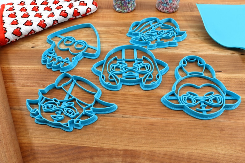 May include: Set of five blue plastic cookie cutters shaped like characters from the video game Splatoon. The characters are wearing hats and goggles.