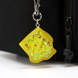 May include: A yellow keychain with a silver clip and a yellow resin charm with glitter and a letter "L" inside.