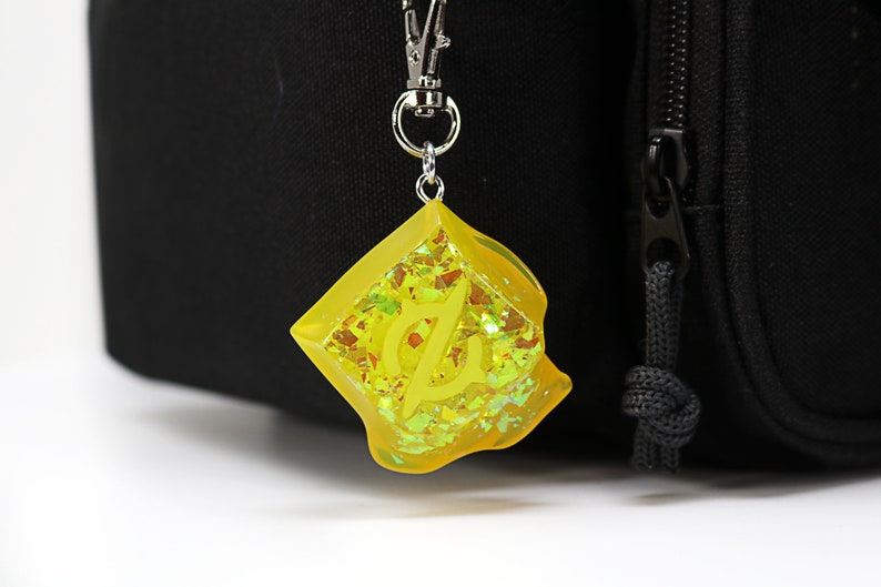 May include: A yellow keychain with a silver clip and a yellow resin charm with glitter and a letter "L" inside.