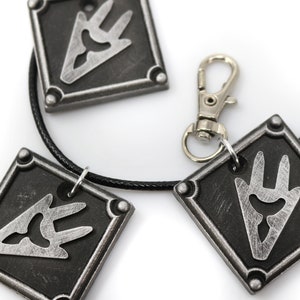 May include: A black necklace with three silver square pendants featuring a stylized silver symbol. The necklace has a silver lobster clasp.