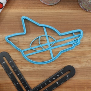 May include: A blue plastic cookie cutter shaped like a cartoon fox head. The cutter has a detailed design with a large eye and a closed mouth.