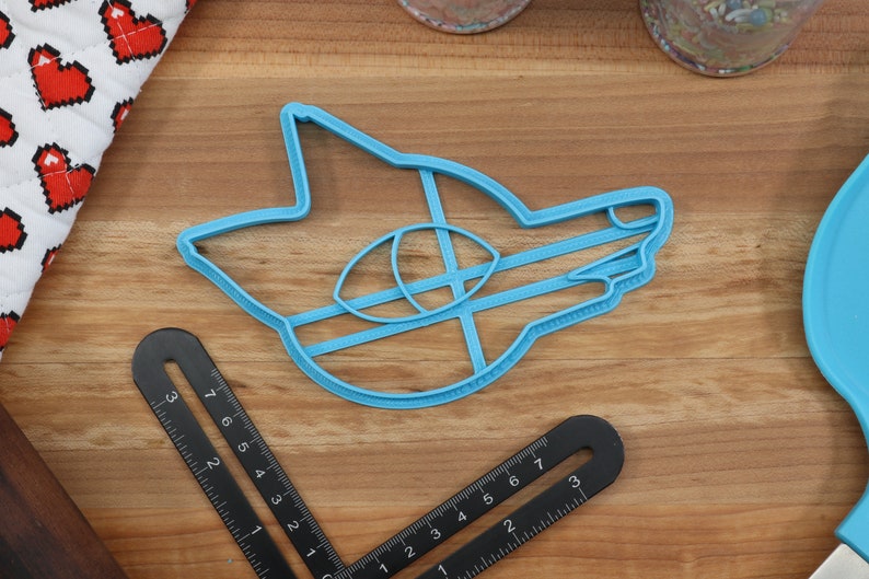 May include: A blue plastic cookie cutter shaped like a cartoon fox head. The cutter has a detailed design with a large eye and a closed mouth.
