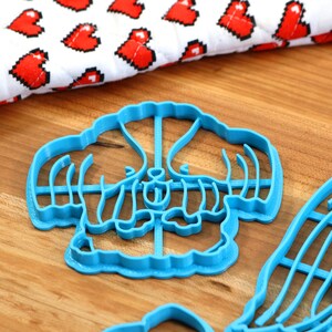 May include: Two blue plastic cookie cutters shaped like a flower and a dog. The cutters are on a wooden surface.