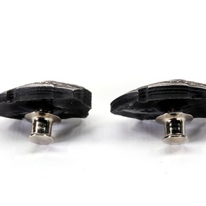 May include: Two black metal buttons with a silver pin and post. The buttons are shaped like a leaf with a textured surface.