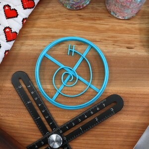 May include: A blue plastic cookie cutter shaped like a circle with a spiral design inside. The cutter has a small handle on the top.