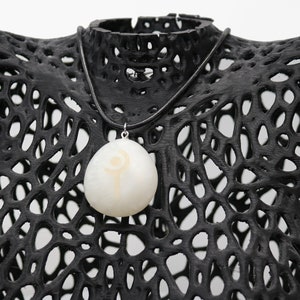 May include: A white pendant necklace with a black leather cord. The pendant is a white stone with a gold symbol on it.