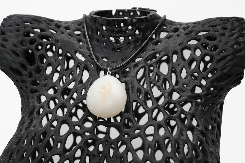 May include: A white pendant necklace with a black leather cord. The pendant is a white stone with a gold symbol on it.