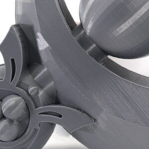 May include: A close-up of a gray 3D printed object with intricate details. The object features a series of rounded protrusions and a curved, flowing design.