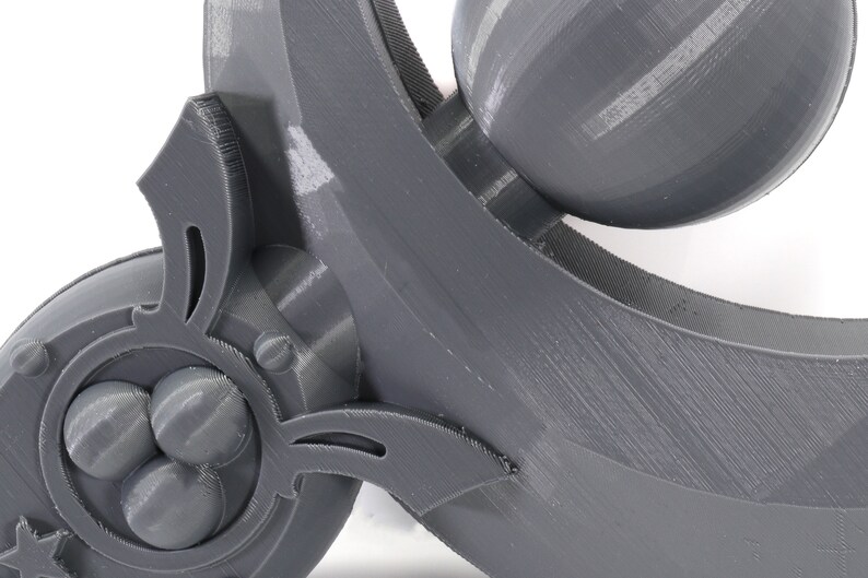 May include: A close-up of a gray 3D printed object with intricate details. The object features a series of rounded protrusions and a curved, flowing design.