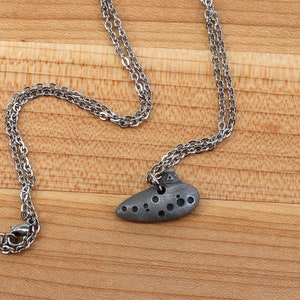 May include: A silver chain necklace with a silver ocarina pendant. The ocarina is a small, wind instrument shaped like a clay pot.
