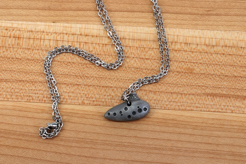 May include: A silver chain necklace with a silver ocarina pendant. The ocarina is a small, wind instrument shaped like a clay pot.