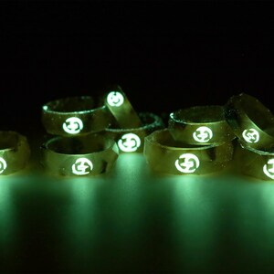 May include: A group of eight gold-colored rings with a glowing green design. Each ring has a white logo in the center.