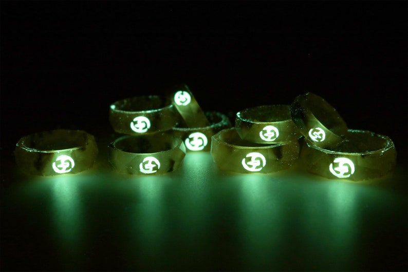 May include: A group of eight gold-colored rings with a glowing green design. Each ring has a white logo in the center.