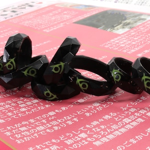 May include: A group of black and green rings with a geometric design. The rings are stacked on top of each other and are made of a shiny material.