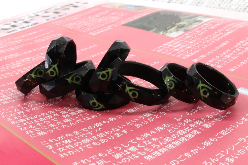 May include: A group of black and green rings with a geometric design. The rings are stacked on top of each other and are made of a shiny material.
