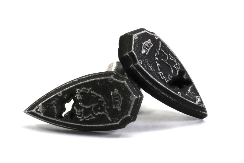 May include: A pair of black metal cufflinks shaped like shields with a silver unicorn design.