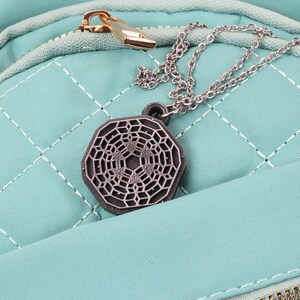May include: A teal quilted backpack with a silver chain and a silver geometric pendant hanging from the zipper.
