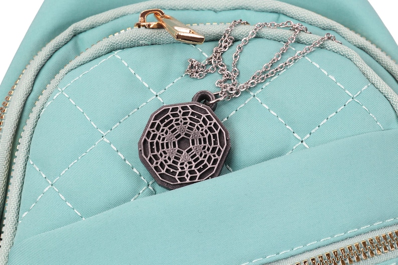 May include: A teal quilted backpack with a silver chain and a silver geometric pendant hanging from the zipper.