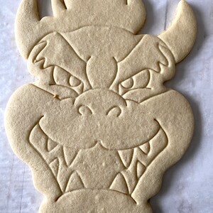 Op de afbeelding: Een simpele suikerkoek in de vorm van een cartoon drakenkop. De koek heeft een gedetailleerd ontwerp met ogen, een mond en hoorns.