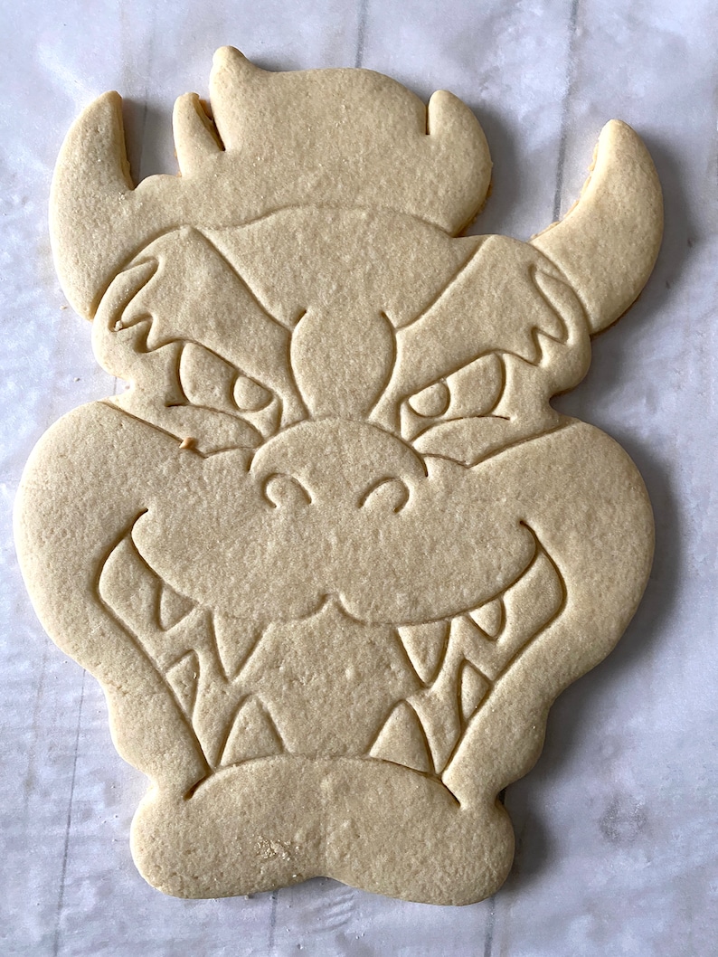 Op de afbeelding: Een simpele suikerkoek in de vorm van een cartoon drakenkop. De koek heeft een gedetailleerd ontwerp met ogen, een mond en hoorns.