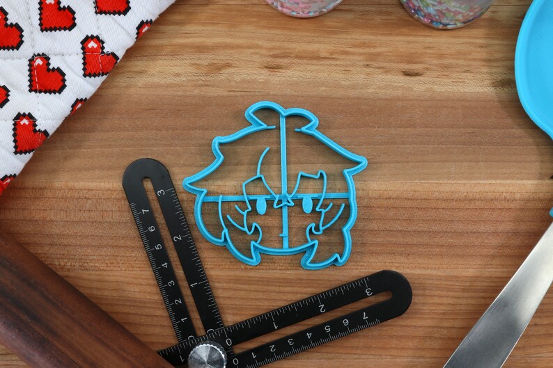 May include: A blue plastic cookie cutter shaped like a cartoon character with a large head and short hair. The character has large eyes and a small mouth.