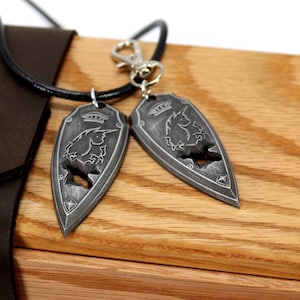 May include: Two silver pendants in the shape of a shield with a unicorn design. The pendants are on a wooden surface with a leather pouch in the background.