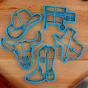Könnte beinhalten: Ein Set mit sechs blauen Plastik-Ausstechformen in Form eines Cowboyhuts, eines Bullenschädels, eines Cowboystiefels, eines Grills und des Bundesstaates Texas.
