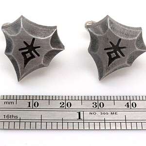 May include: A pair of silver cufflinks with a black kanji character in the center. The cufflinks are about 1 inch in diameter and are shown next to a ruler.