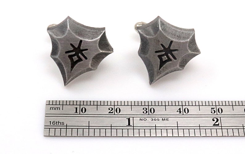 May include: A pair of silver cufflinks with a black kanji character in the center. The cufflinks are about 1 inch in diameter and are shown next to a ruler.