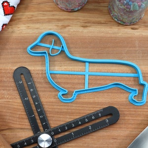 May include: A blue plastic dachshund-shaped cookie cutter on a wooden surface.