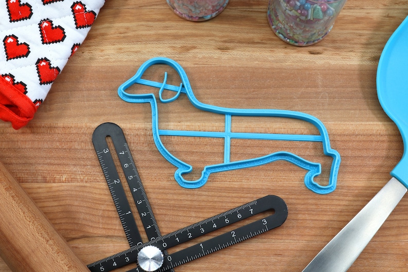 May include: A blue plastic dachshund-shaped cookie cutter on a wooden surface.