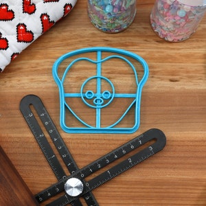 May include: A blue plastic cookie cutter shaped like a slice of bread with a cartoon face. The cutter has a grid pattern and a small nose and eyes.