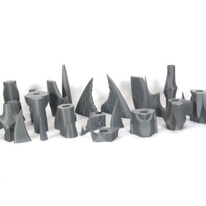 Peut inclure: Un ensemble de 15 pi&egrave;ces en plastique gris imprim&eacute;es en 3D, ressemblant &agrave; des formes pointues, irr&eacute;guli&egrave;res et pointues. Les pi&egrave;ces sont dispos&eacute;es en rang&eacute;e sur une surface blanche.