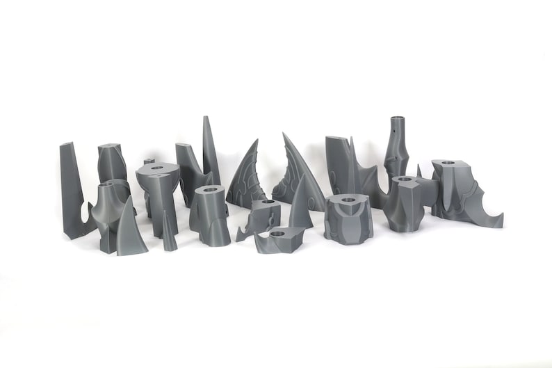 Peut inclure: Un ensemble de 15 pi&egrave;ces en plastique gris imprim&eacute;es en 3D, ressemblant &agrave; des formes pointues, irr&eacute;guli&egrave;res et pointues. Les pi&egrave;ces sont dispos&eacute;es en rang&eacute;e sur une surface blanche.