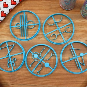 May include: Five blue plastic cookie cutters with different designs. The cutters are on a wooden surface.