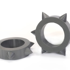 May include: Two grey, 3D printed rings with spikes. The rings are approximately 5 cm in diameter and have 8 spikes each.