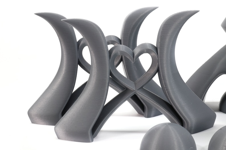 May include: A set of three gray 3D printed sculptures, each featuring a curved shape with a heart design in the center. The sculptures are arranged in a way that creates a sense of balance and harmony.