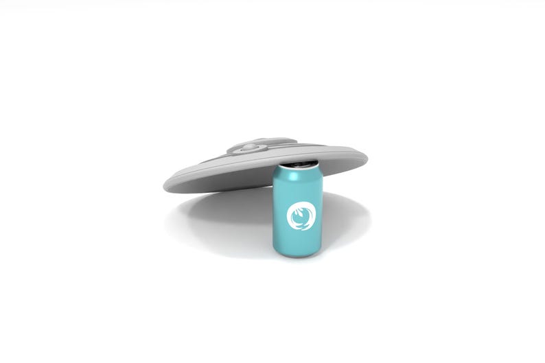 May include: A light blue beverage can with a white logo, positioned beneath a gray, saucer-shaped object. The can is cylindrical and appears to be made of metal. The background is plain white.
