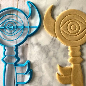 Op de afbeelding: Een blauwe plastic koekjesvormer in de vorm van een sleutel met een oogontwerp en een bruine suikerkoek die met de vormer is uitgestoken.